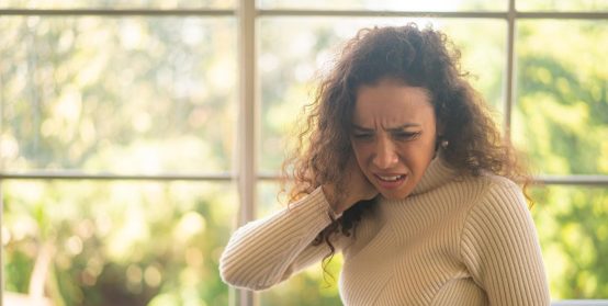 Latin woman sitting on sofa with neckache feeling